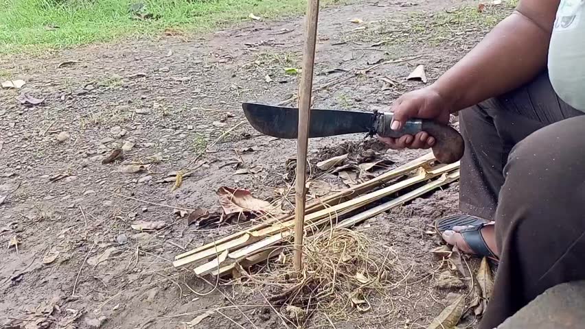 A man doing the process of splitting bamboo with a machete