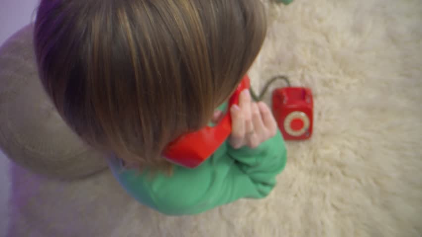 Top-down view of a woman holding a classic red rotary phone to her ear, dressed casually in green and sitting on a plush rug, creating a nostalgic yet modern home ambiance with vintage aesthetics