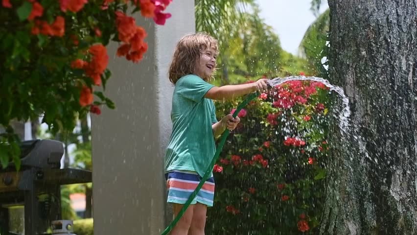 Child planting and watering flowers. Gardening fun with a child. Little one growing plants in the backyard. Summer watering fun with a child. Child playing in the garden with a watering can.