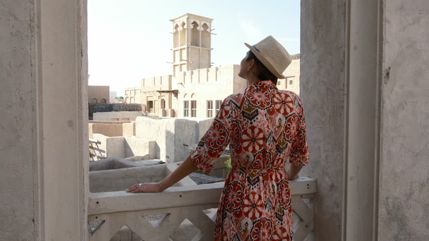 Young woman in ethnic dress and hat exploring Al Seef Park in Dubai. Surrounded by traditional Emirati architecture and modern vibes, she enjoys charm of Dubai Creek's cultural heritage.