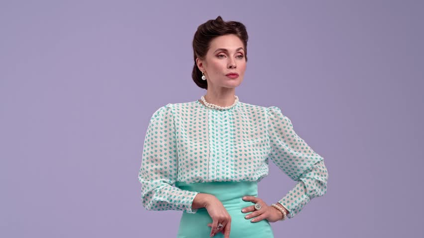 Young woman in vintage outfit and with glamorous hairstyle poses on purple studio background. Beautiful actress in retro style counting, pointing her finger at camera. Beauty and vintage style concept