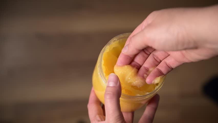 Woman hand taking from jar yellow mango fruit body scrub and show its texture. Rich, tropical exfoliator with zesty texture. Perfect for natural skincare, luxury spa treatments, and beauty rituals. - Powered by Shutterstock - Get 15% off with code: PIKWIZARD15