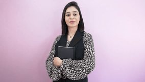 A smiling South Asian young woman looking at camera holding book literature, with positive satisfied face expression, isolated over pink background - Powered by Shutterstock - Get 15% off with code: PIKWIZARD15