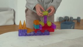 Child assembling a colorful block tower on a white table. The structure features various shapes and vibrant colors. Hands suggest engagement and creativity in indoor play. - Powered by Shutterstock - Get 15% off with code: PIKWIZARD15