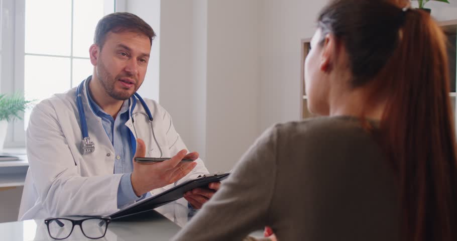 Male doctor consulting female patient, sharing new lab results, positive news, visiting clinic room for medical care, getting health advice, discussing treatment plan, explaining, giving expert advice