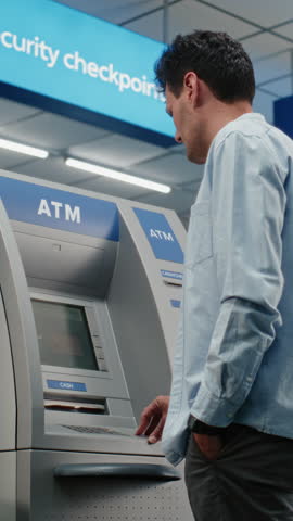 Cash Machine in Crowded Airport Terminal: Man Pressing Buttons on ATM Keypad, Entering PIN Code for Cash Withdrawal Transaction, Taking Money. Automated Teller Machine, Banking Services. Vertical Shot