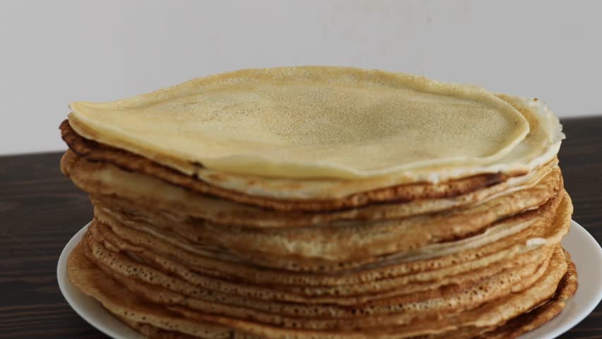 folding thin crepe from tall stack into triangle shape over white plate on dark wooden table, concept of breakfast preparation, traditional homemade pancakes, cozy culinary ritual