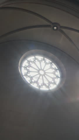 Vertical no people shot of dark catholic church interior lit by sunrays streaming through exquisite round stained glass window under Gothic vaults