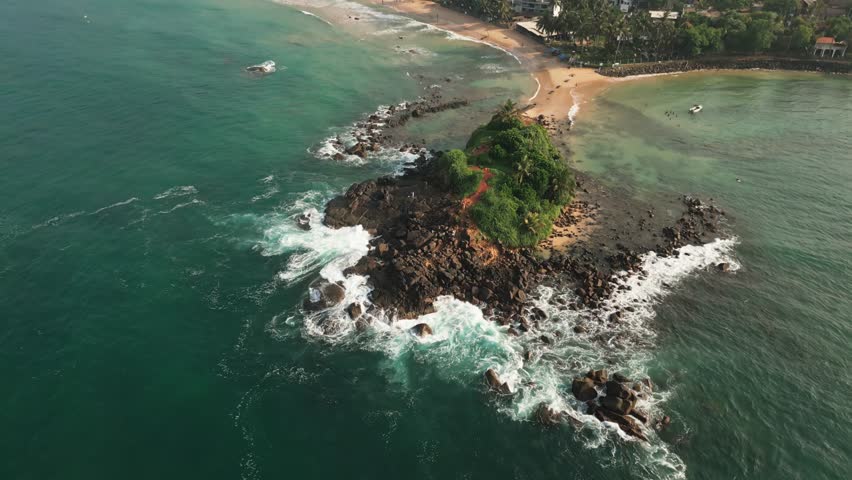 Aerial fly over view Mirissa Beach and Parrot Rock, showcasing pristine turquoise waters, golden sandy shores, rocky coastal formations, southern Sri Lanka. Vibrant tropical landscape indian ocean