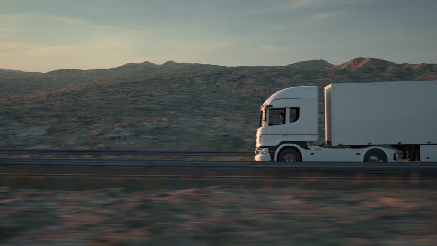 Side view of a white long distance semi truck with cargo trailer drives on a desert road into the sunset. Drone POV following the truck. 3d animation rendering.