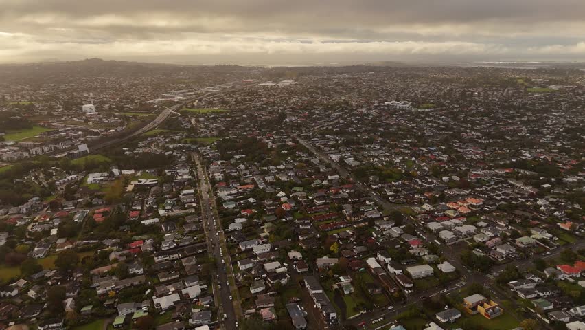 Aerial establishing shot of Auckland city with ocean in background. Cloudy sunset time on New Zealand island. Houses, Buildings and neighborhood on island. Panning shot.
