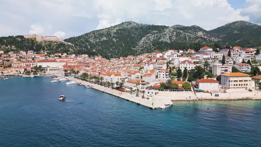 Hvar, Croatia from above with showing the rising rows of houses on a Spring day. Sailboats and yachts line the dock. Sailboats and yachts line the dock and the mountains line the background.