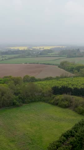 Portrait Drone over English fields, trees and distant rapeseed under cloudy grey skies