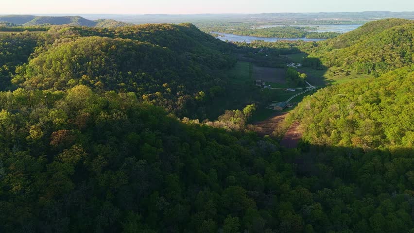 Aerial video from Apple Blossom Overlook Park showing green rolling hills and the Mississippi River at sunset with glowing sky and peaceful scenery.