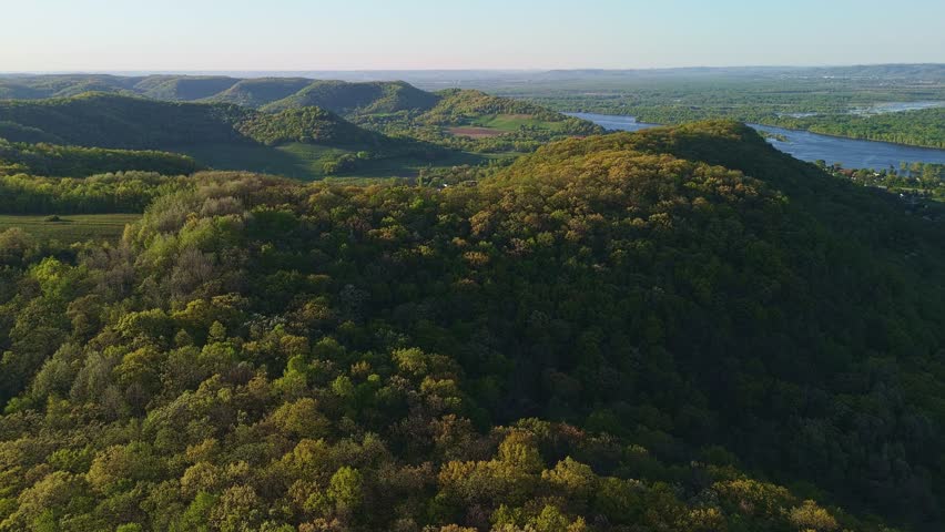 Aerial video from Apple Blossom Overlook Park showing green rolling hills and the Mississippi River at sunset with glowing sky and peaceful scenery.