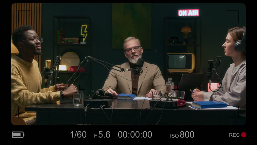 Camera recording screen view of mature Caucasian guest talking with young diverse hosts sitting at table during podcast show