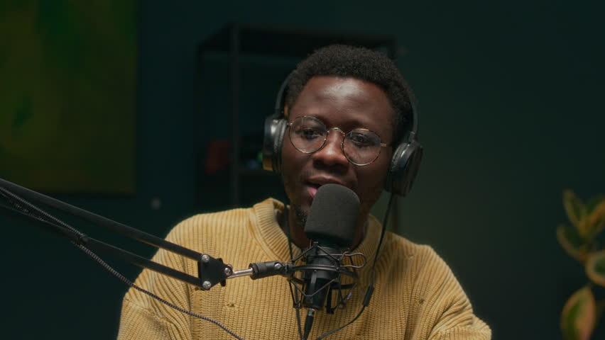 Handheld shot of young African American host talking to adult Caucasian male influencer in microphone during podcast recording in studio
