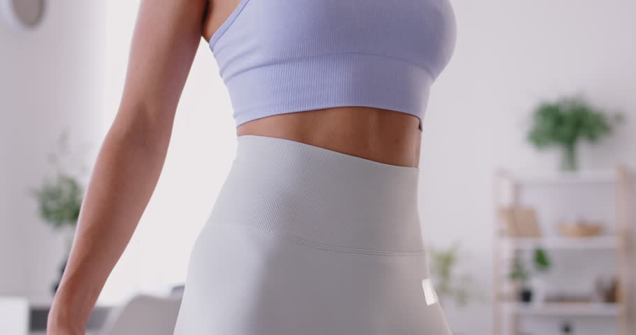 Slow motion video of faceless slim sporty woman wearing sportswear measure the waist with measuring tape standing at home. Slimming, sport, diet and weight control concept. 4k video.