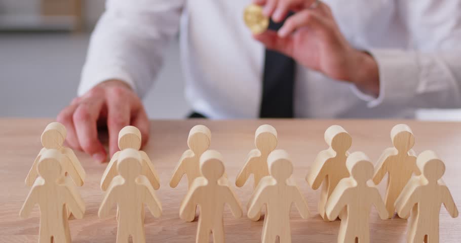 Young man holding bitcoin in hands in front of wooden figures of people at the desk. Businessman trading on stock market. Digital money, cryptocurrency and business concept. 4k video.