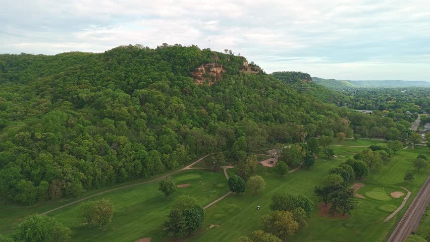 Drone video of Grandad Bluff at sunset overlooking La Crosse Wisconsin with glowing sky, city view, and scenic sandstone cliff formation.