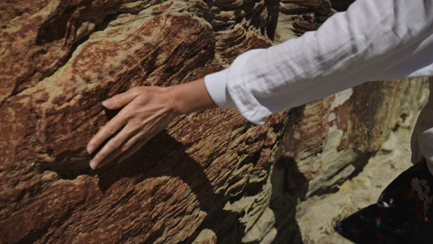 A female hand glides over textured sandstone rocks, capturing the rough tactile sensation and geological volume of the material.