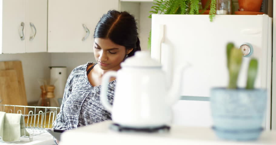 woman interacting with tablet in home kitchen, displaying floating social media pop-up labels. Technology, lifestyle, minimalism, household, communication, modern, cozy