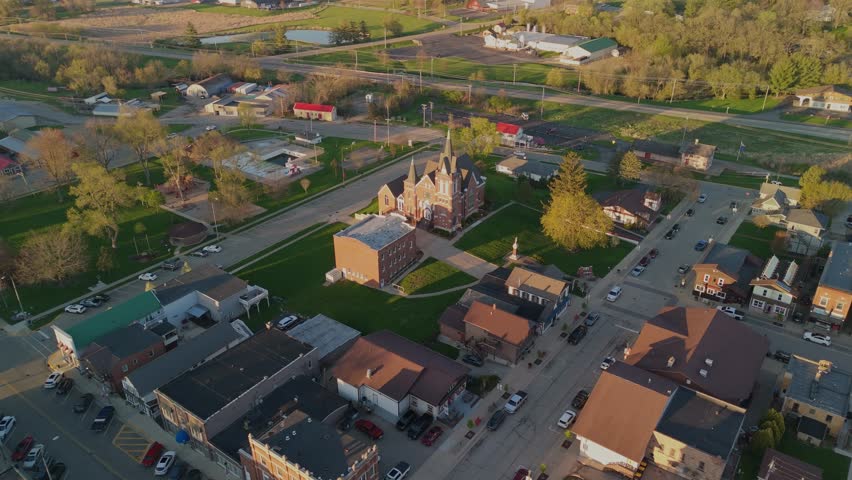 Drone video flying over New Glarus Wisconsin at sunset showing city buildings, rooftops, and the Swiss United Church of Christ in golden light.