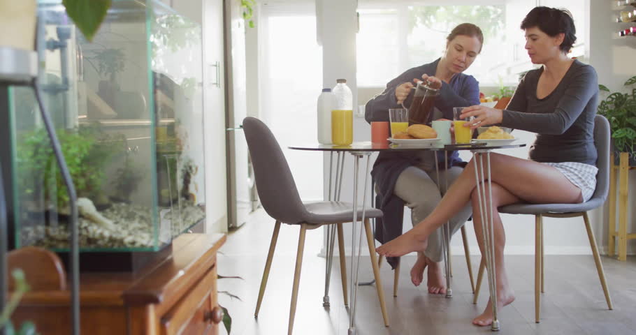 Two marketers pouring coffee at table in kitchen, displaying floating social media marketing icons. Candid, social, vibrant, lifestyle, casual, contemporary, communication