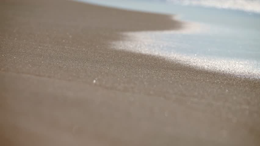 Soft morning light dances on gentle waves near tranquil shoreline. Shimmering reflections create calming, sparkling effect on serene beach. Warm tones emphasize early hours and peaceful ambiance