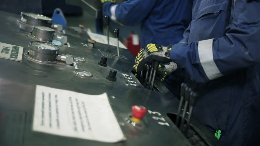 Workers operating drill testing control panel at oil facility