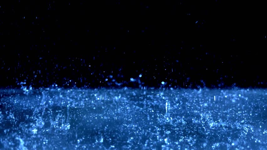 Slow motion close-up of raindrops falling and splashing on a dark surface, creating ripples and droplets in moody lighting.