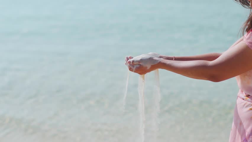 Close up of woman Hand releasing dropping sand and beach in background. Sand flowing through the hands. Summer beach holiday vacation concept.