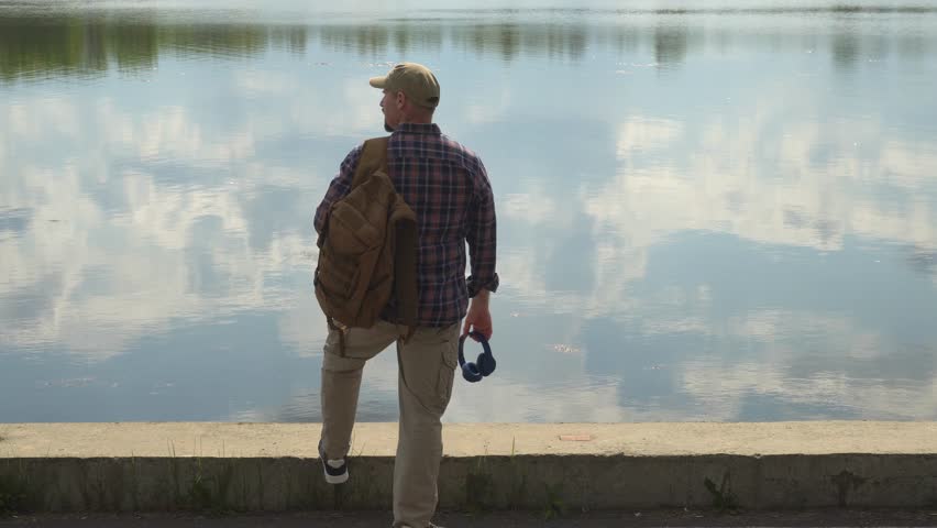 Tourist looking at lake reflecting clouds on sunny day