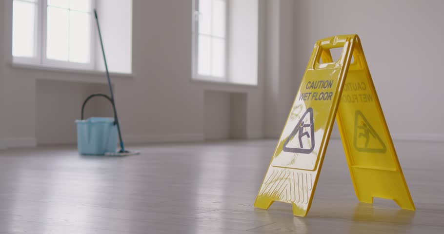 Caution wet floor sign with cleaning tools and a bucket in empty room or office in background. Cleaning service, housekeeping and household work concept. 4k video. Slow motion video.