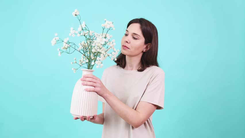 Woman smelling white flowers in vase on turquoise background