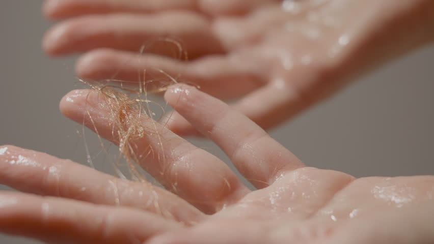 Hands are shown in a close-up as they wash hair in the shower. Hair strands fall into the palms, illustrating the struggle with hair loss and weak hair during washing.