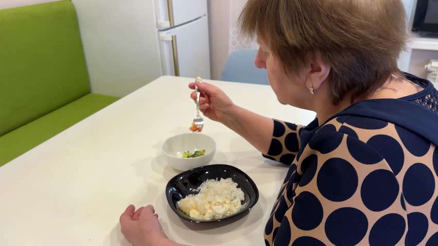 An elderly lady enjoys her meal at the table, taking her time to appreciate the flavors.