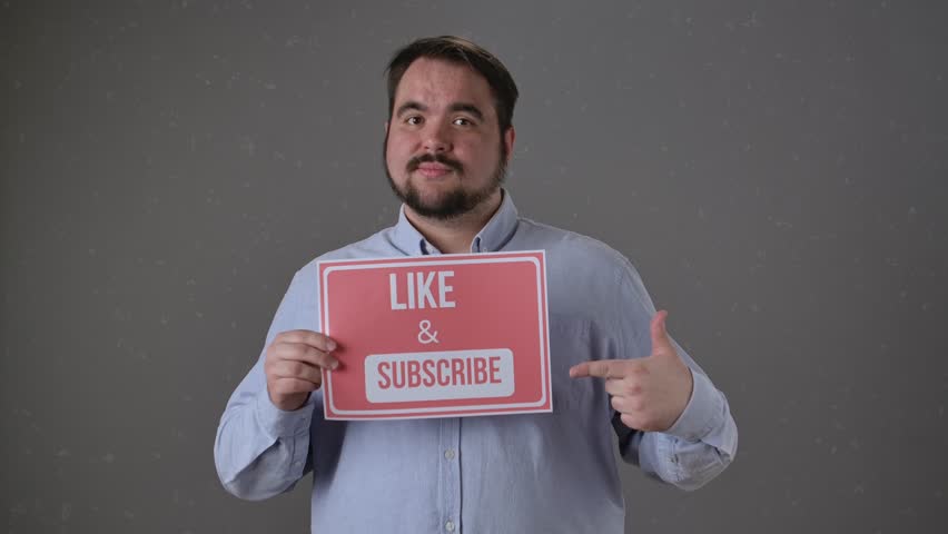 A person holds a sign that reads Like and Subscribe, pointing to it, encouraging viewers to engage with content.