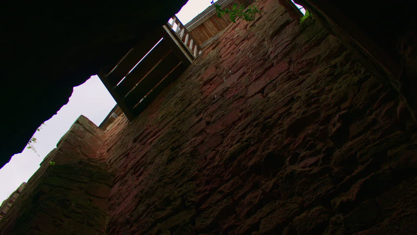 Tilt shot of a weathered stone wall and a small inner bridge of a medieval castle. Between the inner walls of an ancient castle.