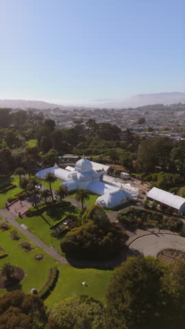 Aerial footage of landscaped garden with a stunning white Conservatory of Flowers at Gardens of Golden Gate Park in San Francisco surrounded by tall palm trees and colorful flowers. California, USA
