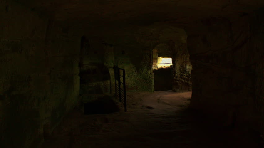 First person view of walking towards grated windows inside of a dimly lit room of an ancient castle. The interior of a dark castle room with two small grated windows.