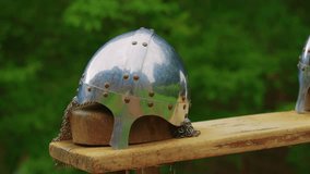 Close-up shot of a shiny medieval helmet crafted from polished metal, sitting atop a wooden platform. The helmet features a rounded top and is adorned with chainmail coif - Powered by Shutterstock - Get 15% off with code: PIKWIZARD15