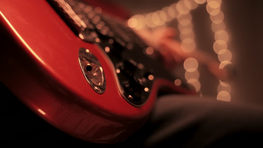 A man is turning the volume knob on an electric guitar and start playing. Close up view