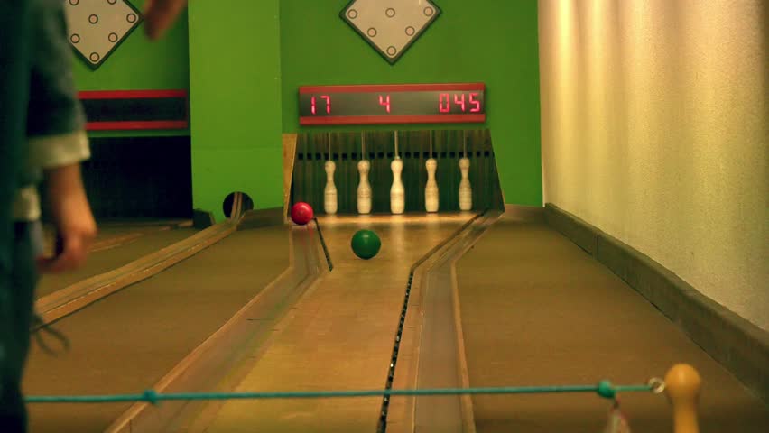 Bowling alley scene featuring a wooden lane, electronic scoreboard, and fallen pins. The green and white backdrop adds a retro vibe to the competitive scoring display.