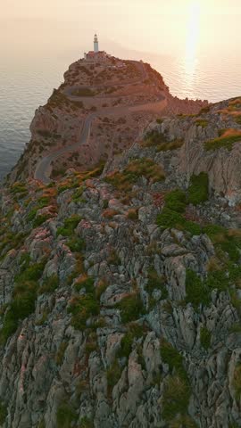 Aerial view of the picturesque lighthouse at Cape Formentor at sunrise, Mallorca, Balearic Islands, Spain. A beautiful winding road leads to the scenic lighthouse perched on a high cliff above the sea