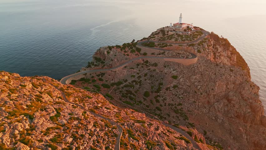 Aerial view of the picturesque lighthouse at Cape Formentor at sunrise, Mallorca, Balearic Islands, Spain. A beautiful winding road leads to the scenic lighthouse perched on a high cliff above the sea