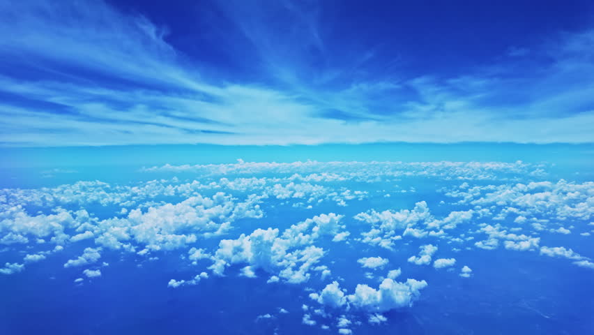 View from airplane window scattered white clouds floating above a vast landscape, with winding rivers below. The deep blue sky and soft cloud formations create a sense of serenity and vastness.