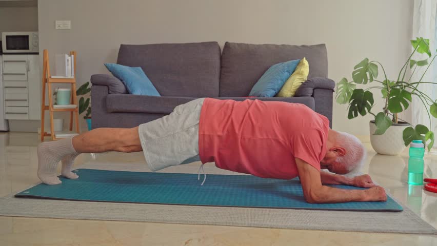 Video of Senior man doing plank exercise on fitness mat at home