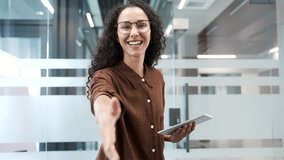 Happy young businesswoman extending her hand to say hello while standing in modern business office. Smiling positive female manager in glasses with digital tablet in hands looking friendly at camera - Powered by Shutterstock - Get 15% off with code: PIKWIZARD15