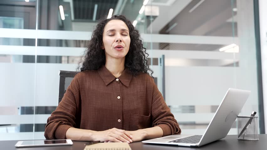 Young businesswoman relaxing breathing deeply while sitting at a desk at a workplace in a business office. Calm happy female employee resting with her eyes closed. Joyful woman took a break from work